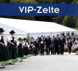 Großes weißes VIP-Zelte mit prominenten Gästen davor und jungen Trachtlerinnen, die Spalier stehen.